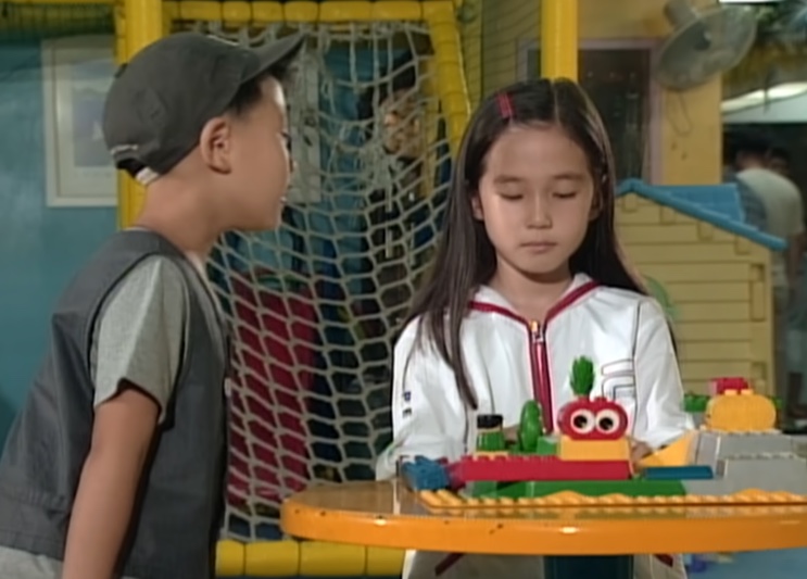 Su-ji e Jung-bae frente a frente numa mesinha de parquinho coberta de peças de montar