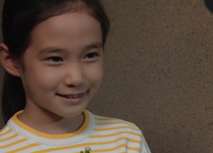 Su-ji sorrindo de leve, de blusa listrada de amarelo