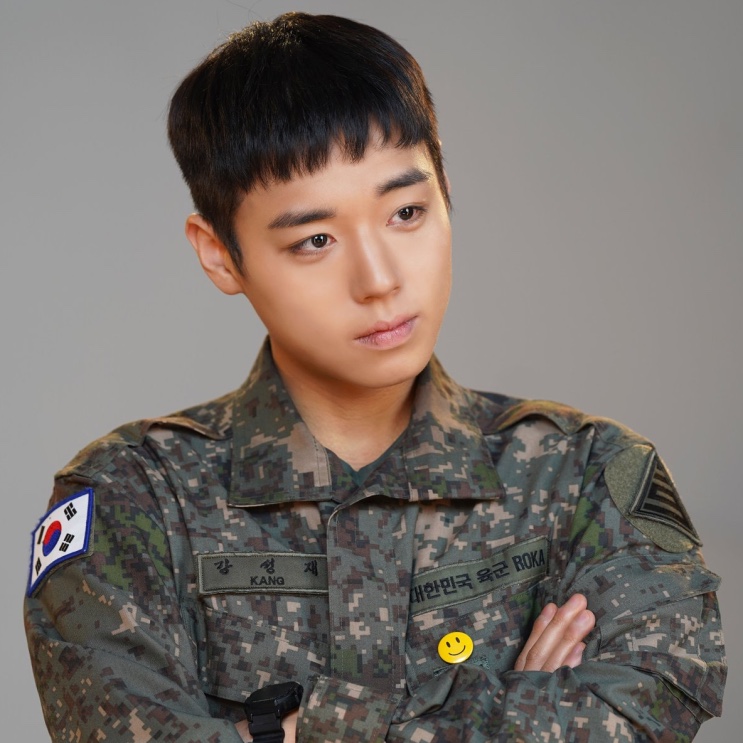 Park Ji-hoon de farda camuflada do Exército coreano, de braços cruzados