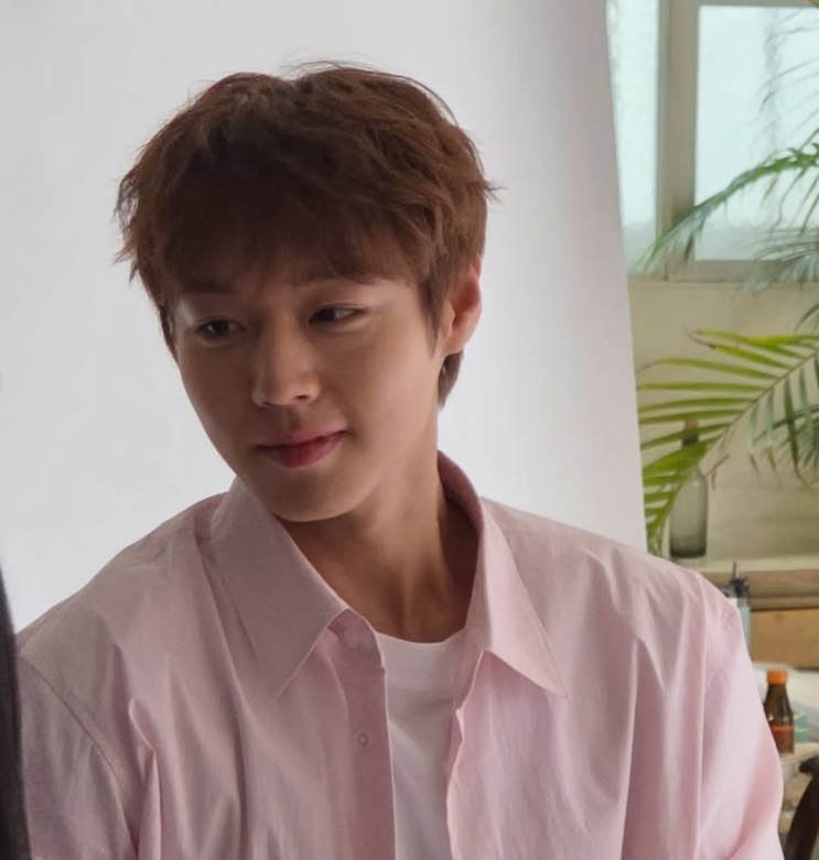 Park Ji-hoon de camisa rosa-clara, sorrindo de lado