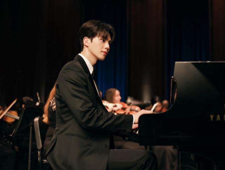 Rapaz tocando piano de cauda diante de uma orquestra, em um palco