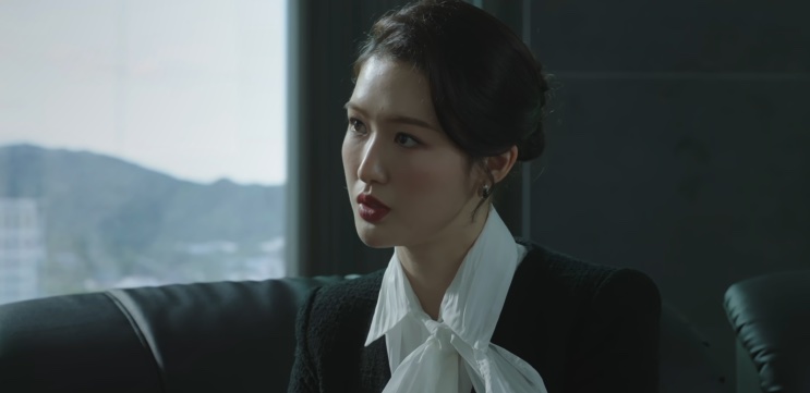Jin Ye-jun sentada em uma poltrona de escritório, com expressão séria