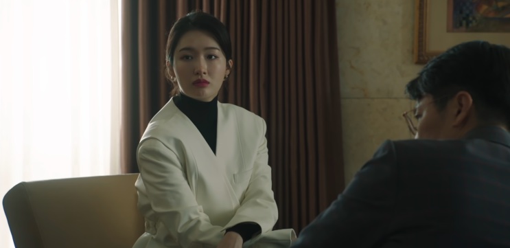 Jin Ye-jun de terno claro, conversando com um homem sentado à sua frente