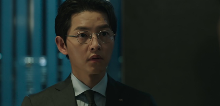 Yoon Hyun-woo de óculos e terno, falando em um ambiente de escritório