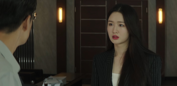 Jin Ye-jun de terno risca de giz, de pé em um ambiente interno