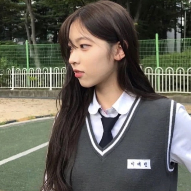 May, do Rescene, de uniforme escolar com colete cinza e gravata, numa quadra de escola