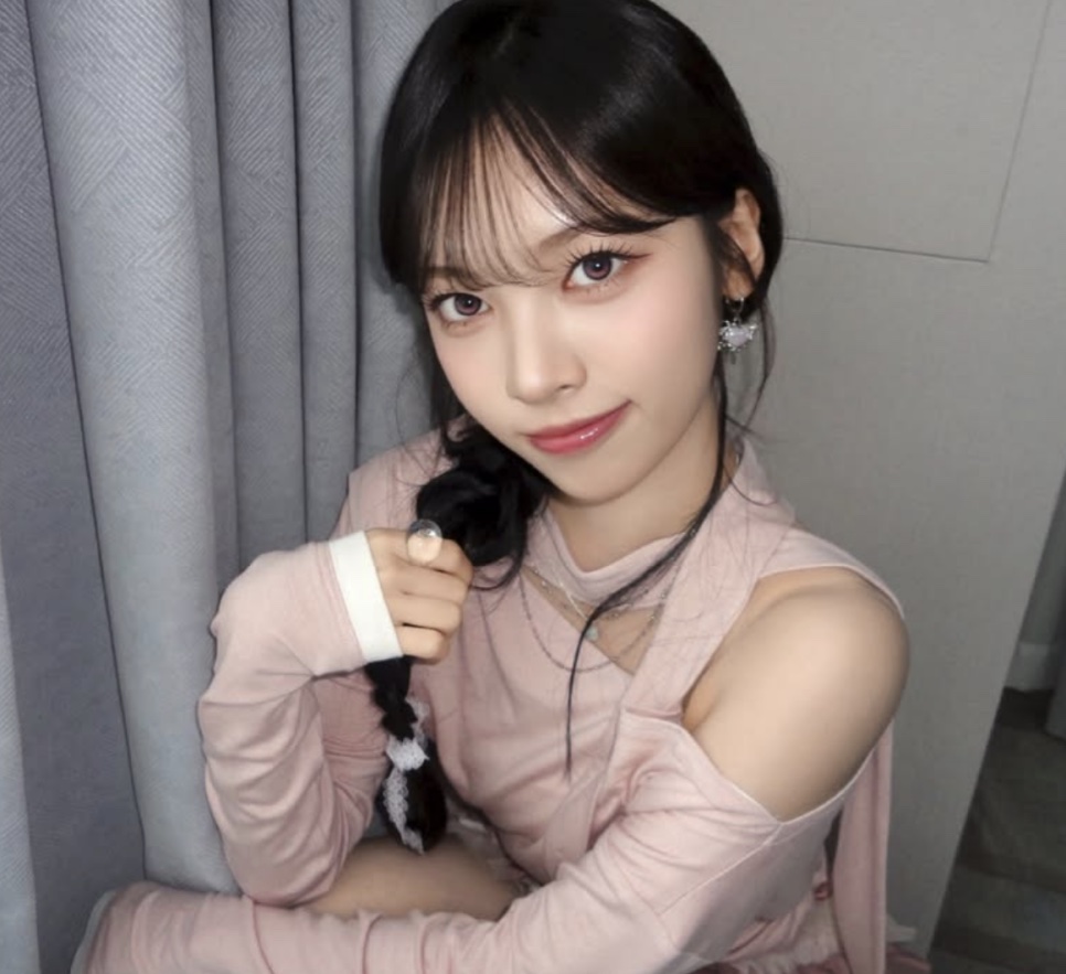 May, do Rescene, de blusa rosa, segurando uma trança do próprio cabelo