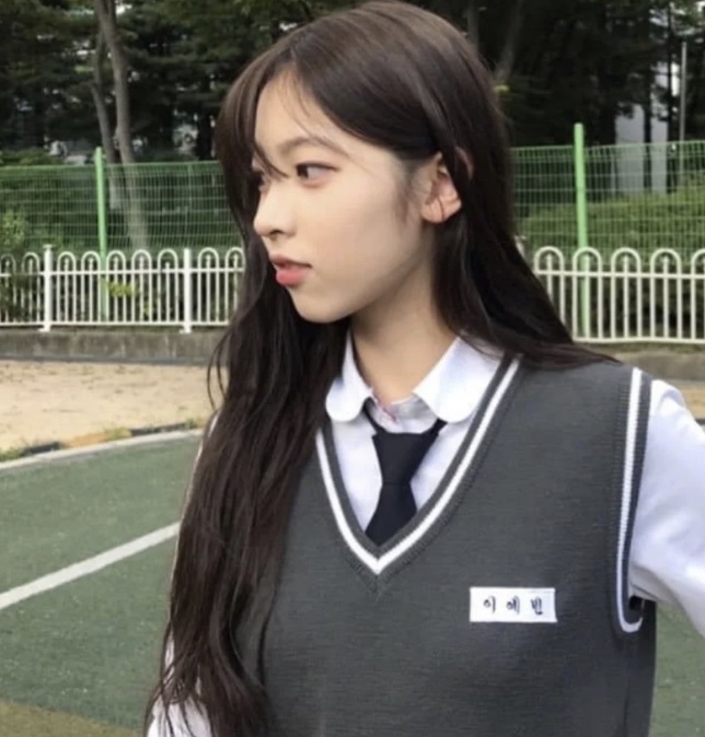 May de perfil, de uniforme escolar com o nome bordado no colete