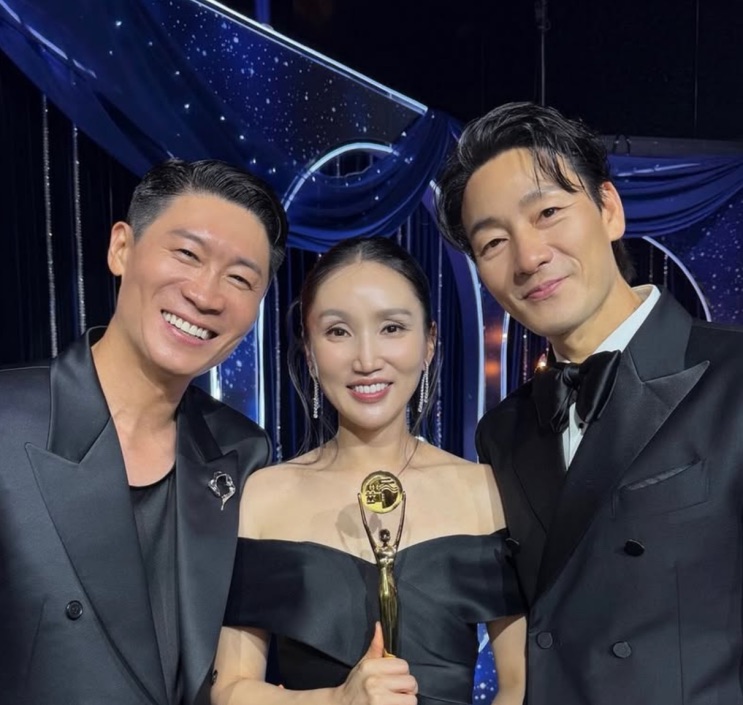Park Bo-kyung no palco com o troféu, entre dois apresentadores de terno
