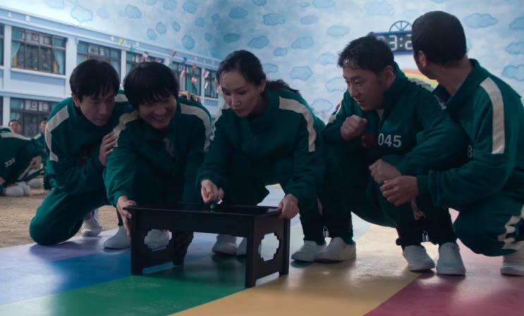 Participantes com as pernas amarradas agachados diante da mesinha de uma das provas