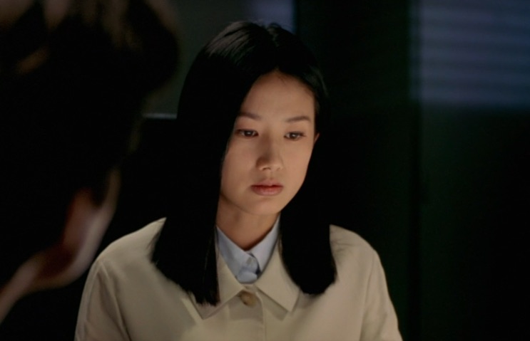 Shim Eun-ha de perfil num corredor escuro, de blusa clara