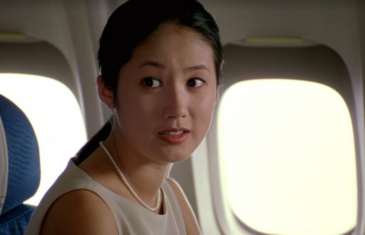 Shim Eun-ha sentada junto à janela de um avião, olhando para trás