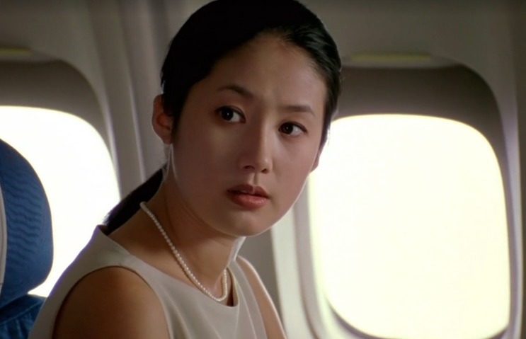 Shim Eun-ha encostada na janela do avião, de blusa branca