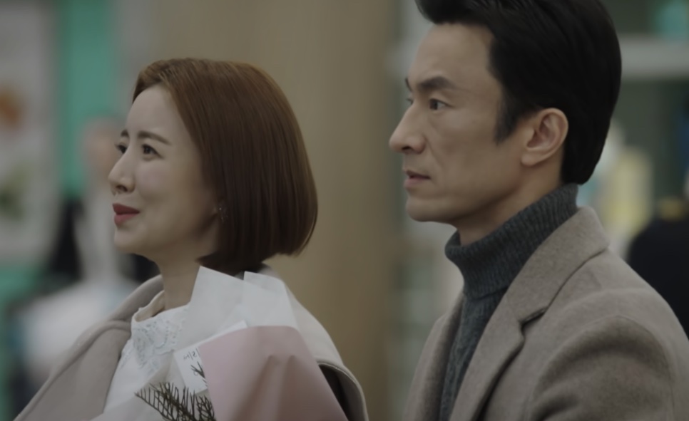 Os pais da Se-ri, No Seung-hye com um buquê de flores e Cha Min-hyeok, esperando no aeroporto