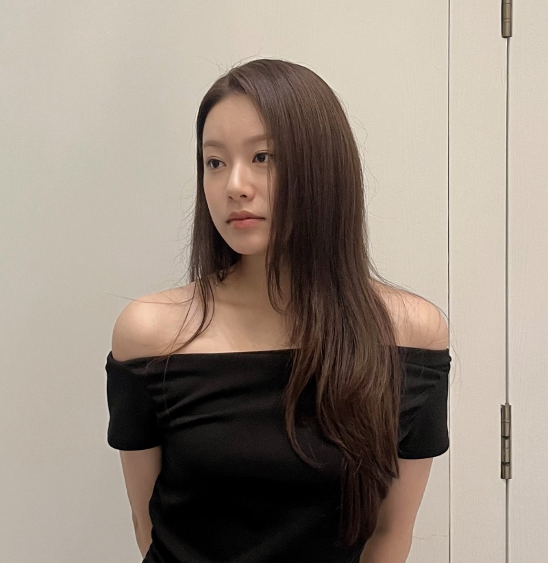 A atriz Park Yoo-na, intérprete da Cha Se-ri, de blusa preta de ombro a ombro, encostada numa parede