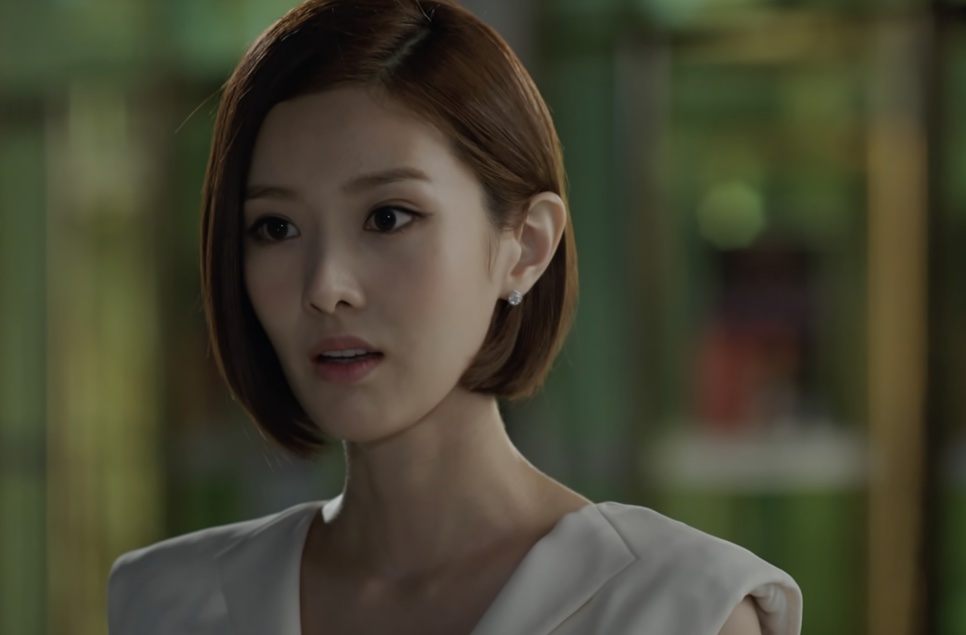 Tae Yi-ryung de blusa branca conversando, com um jardim de vidro ao fundo