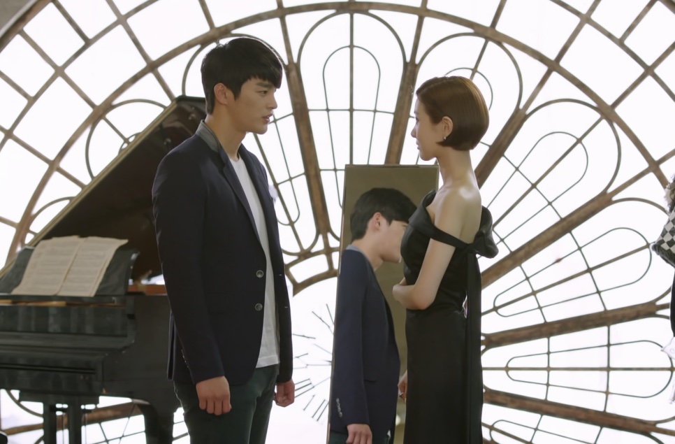 Kang Woo, personagem de Seo In-guk em Sol do Mestre, de frente para Tae Yi-ryung em um salão com piano e janela em arco
