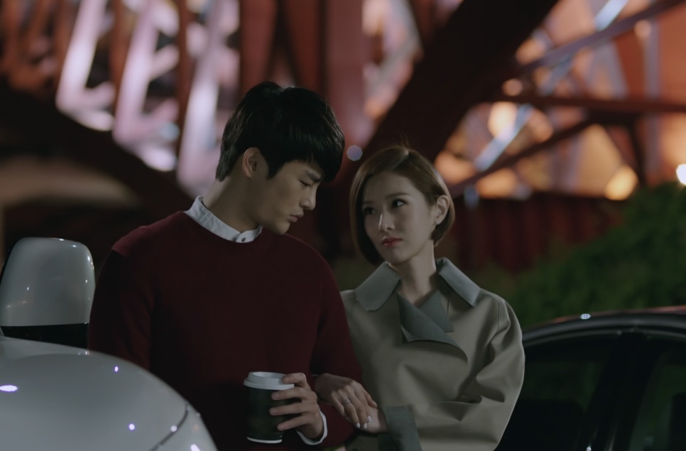Kang Woo de suéter vinho com um copo de café na mão, ao lado de Tae Yi-ryung, perto de um carro branco à noite