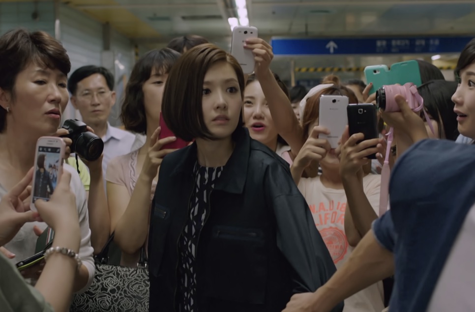 Tae Yi-ryung no meio de uma multidão que a cerca com celulares e câmeras
