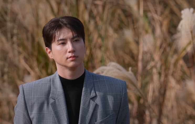Choi Hyuk-jun de terno, em pé no meio do capim prateado