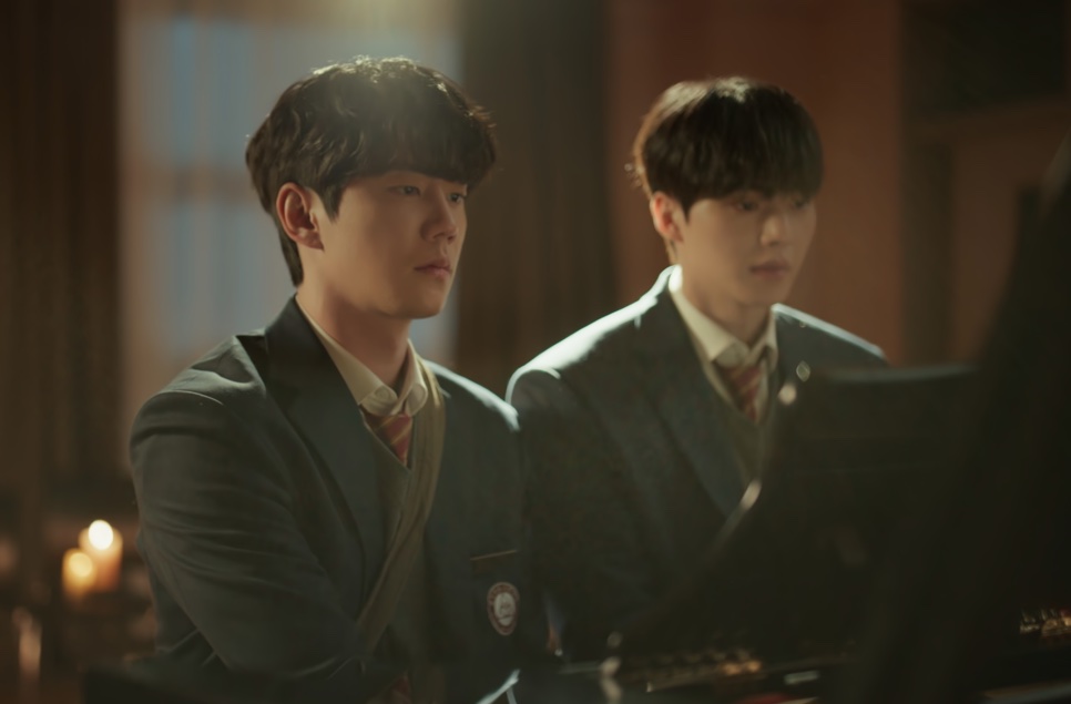 Os dois protagonistas de Quatro Mãos, Duas Sonatas, de uniforme escolar, sentados lado a lado diante de um piano, à luz de velas