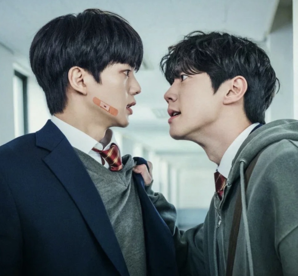 Kang Pi-o (Song Kang) e Choi Jeong-yo (Lee Jun-young), de uniforme escolar, cara a cara num corredor, um segurando o paletó do outro