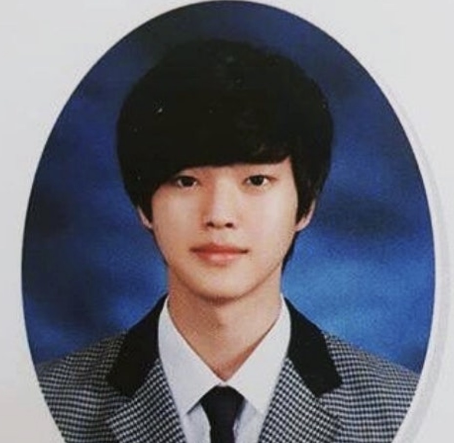 Foto antiga do Song Kang adolescente, de uniforme escolar e gravata, em moldura oval