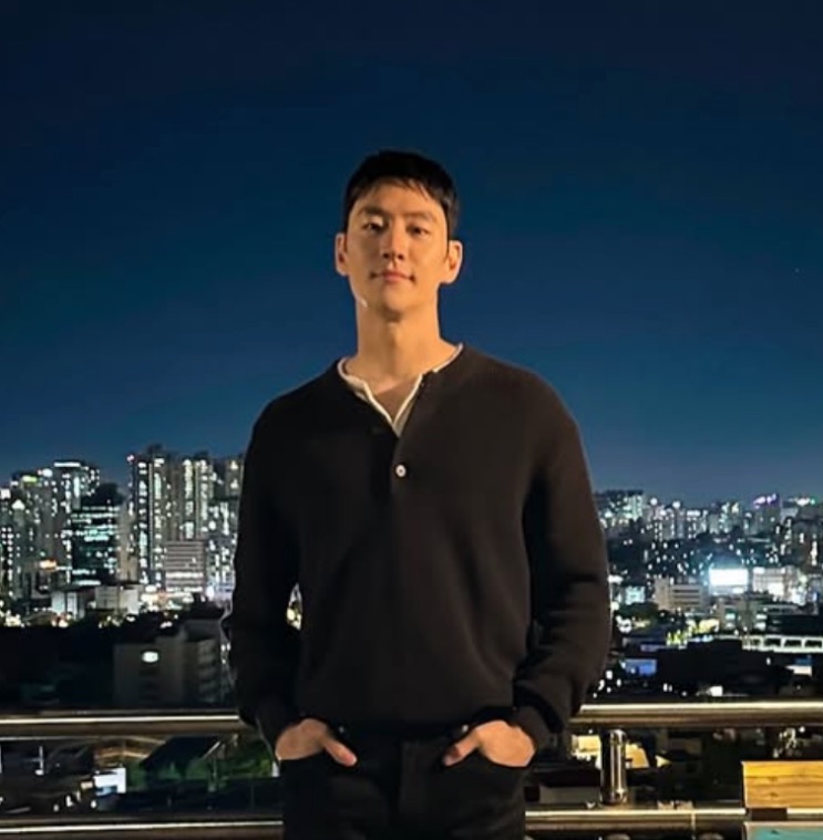 Lee Je-hoon com a cidade iluminada ao fundo