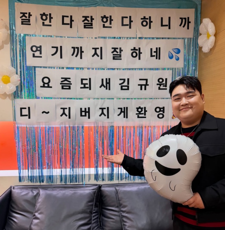 Kim Kyu-won posando ao lado de um painel feito por fãs
