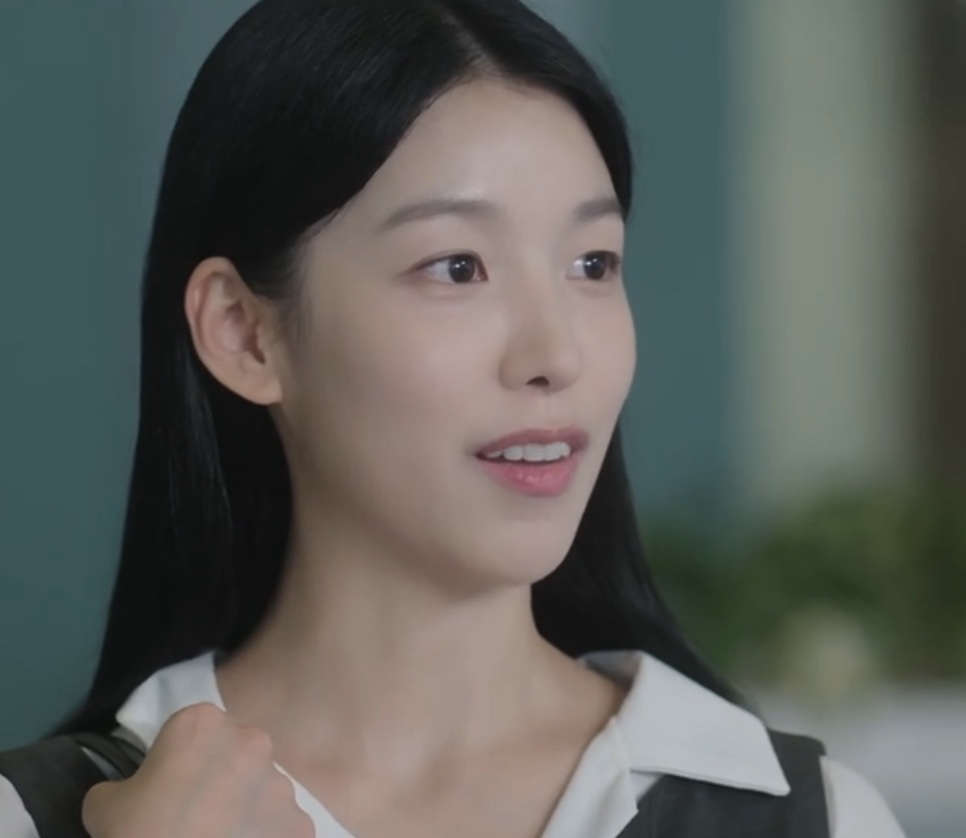 Jang Hyang-eun, personagem da Baek Yae-in em The Ordinary Jackpot, sorrindo de blusa branca e colete escuro
