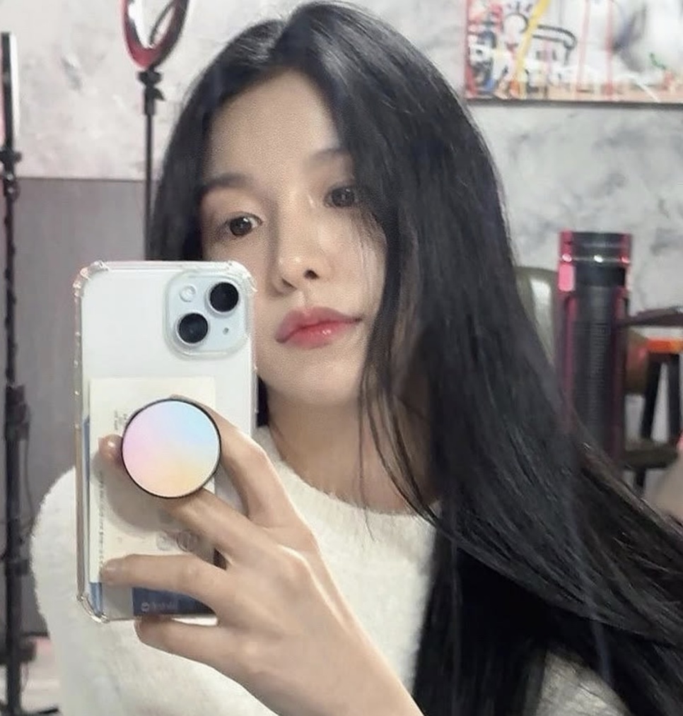 A atriz Baek Yae-in de suéter branco, tirando selfie com o celular