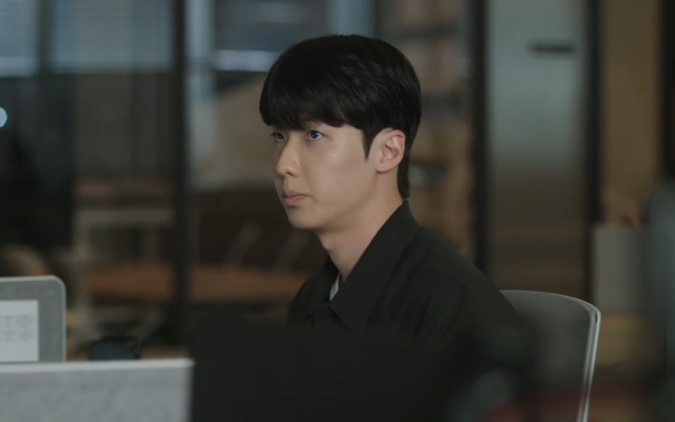 Park Ki-tae, de camisa preta, sentado à mesa no escritório em The Ordinary Jackpot