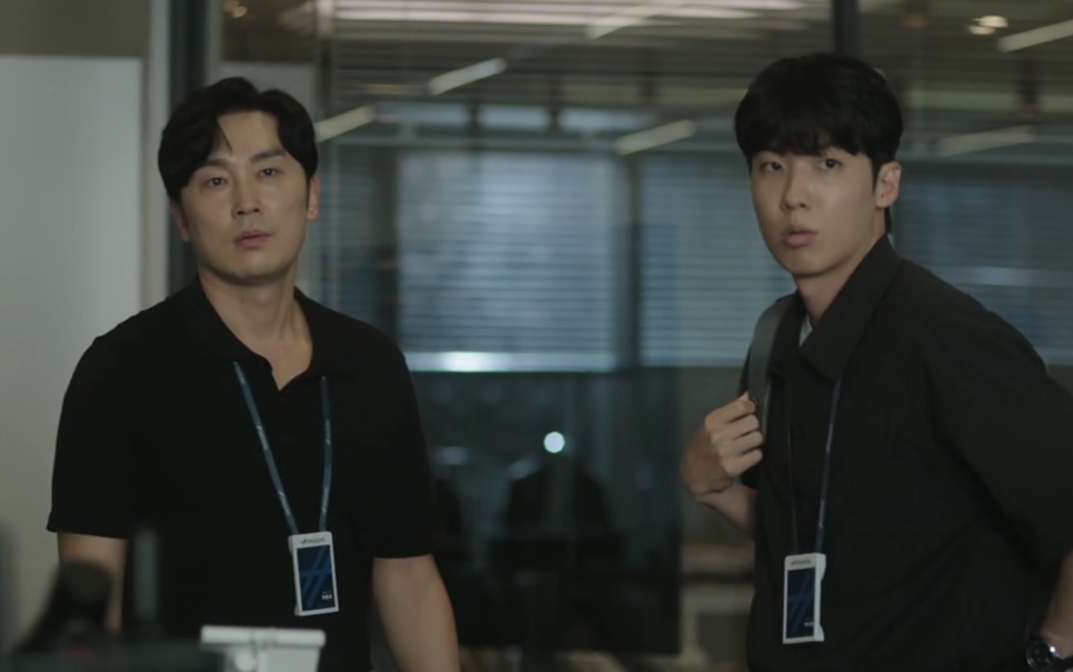Park Ki-tae, de mochila e crachá, ao lado de um colega no escritório em The Ordinary Jackpot