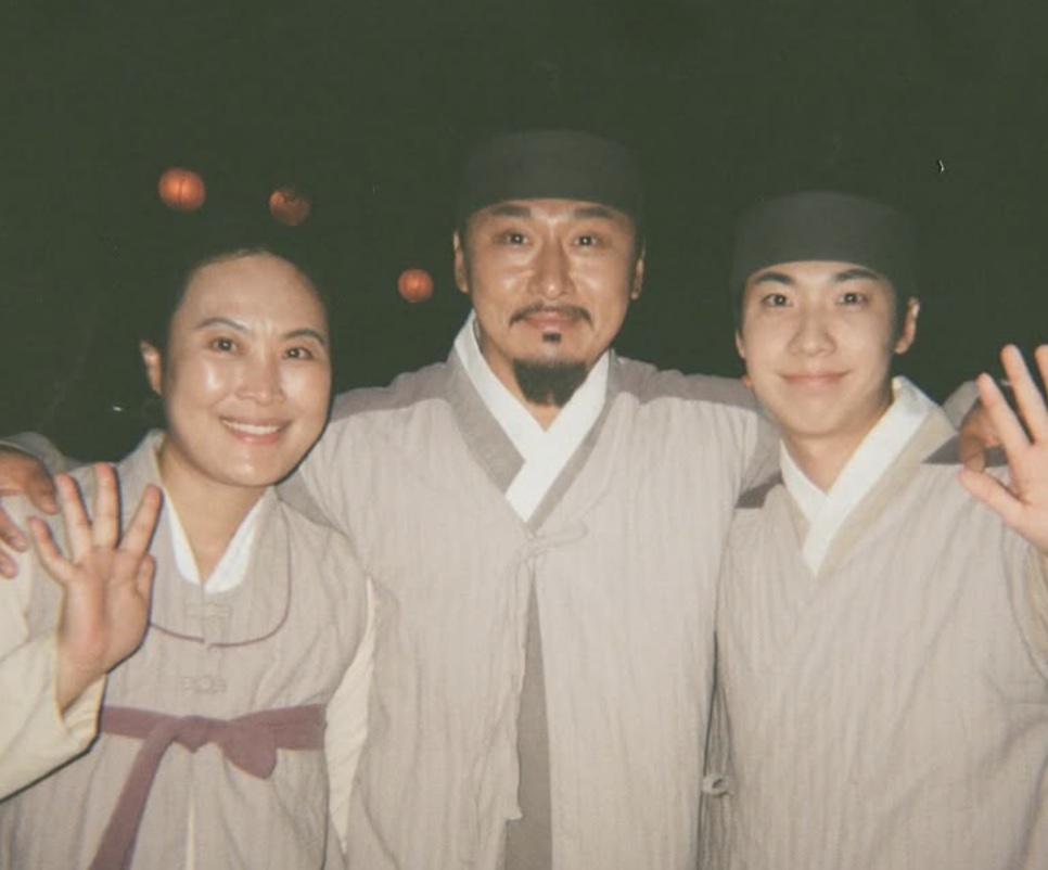 O ator Hong Jin-gi com figurino de época, posando com dois colegas de elenco nos bastidores