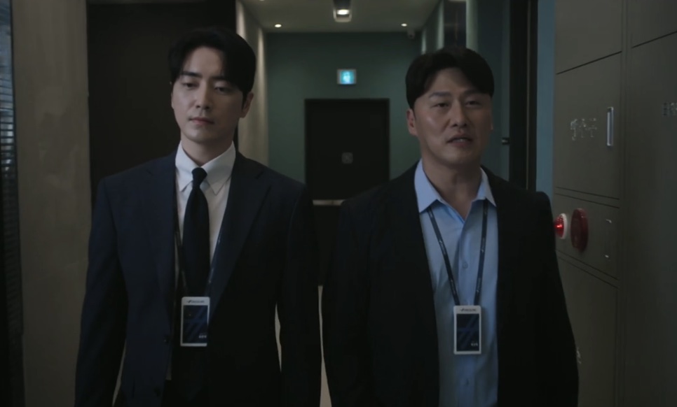 Gong Eun-tae e Jung Seon-hyuk, os dois de terno e crachá, andando lado a lado num corredor em The Ordinary Jackpot