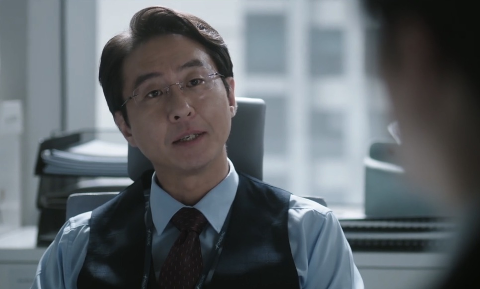 Close do Jang Kyung-chul, de óculos, falando com alguém à mesa dele em The Ordinary Jackpot