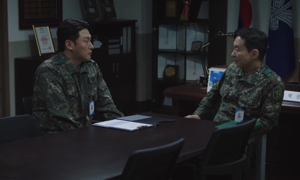Dois oficiais de uniforme camuflado conversando numa sala de reunião do quartel em New Recruit 4