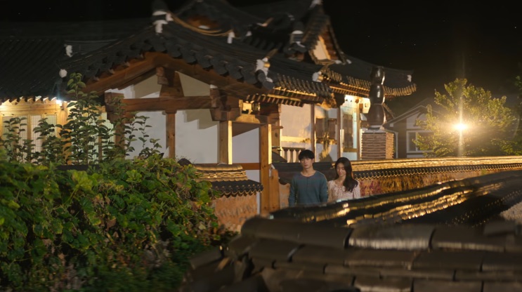 Casa hanok iluminada à noite, com duas pessoas ao fundo