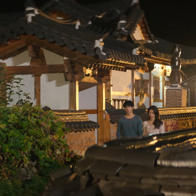 Telhado de hanok à noite, com Tae-ha e Eun-sae ao fundo