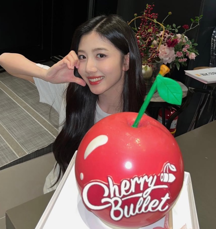 Choi Yu-ju ao lado de um bolo do Cherry Bullet