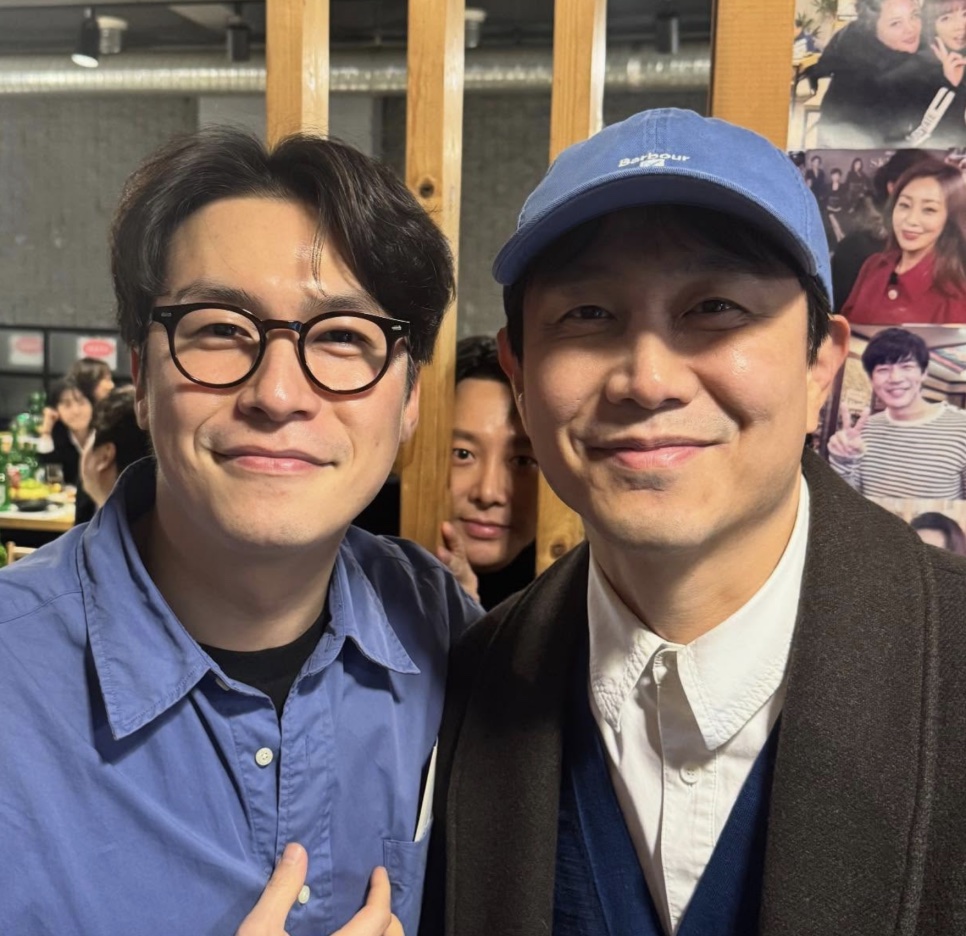 Lee Jae-won de óculos redondos ao lado do Oh Jung-se, de boné azul, em um restaurante