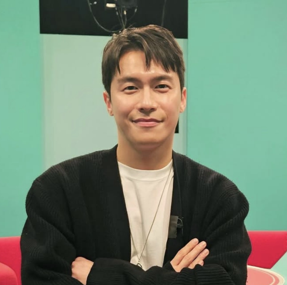 Lee Jae-won de braços cruzados, de cardigã preto, em um estúdio