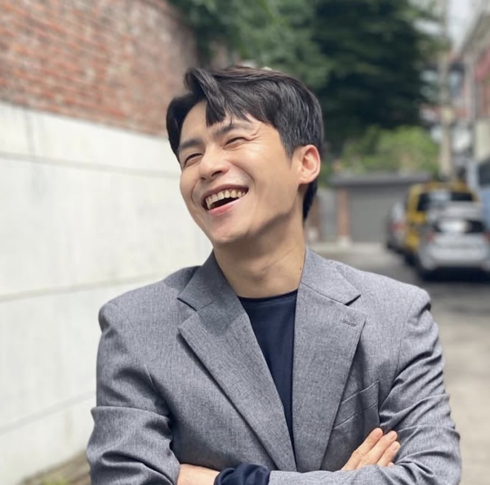 Lee Jae-won rindo, de terno cinza, na rua