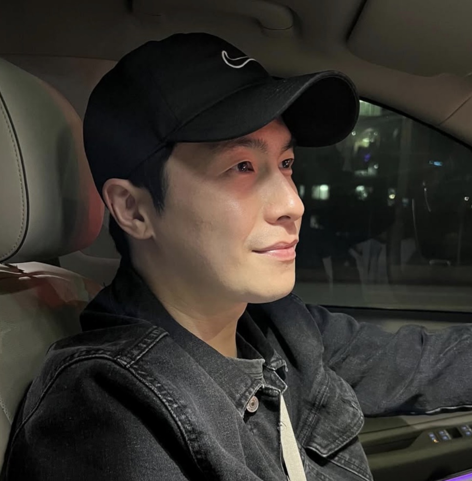 Lee Jae-won de boné, dentro do carro, olhando pela janela