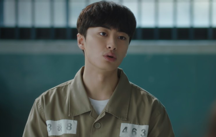 Yang Jeong-il de uniforme de detento, com o número preso à roupa, falando de frente