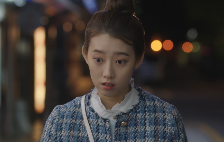 Shin Hye-young falando na rua à noite, com luzes desfocadas ao fundo