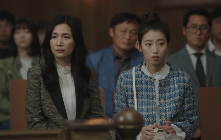 Shin Hye-young sentada na plateia do tribunal ao lado da mãe, entre outras pessoas