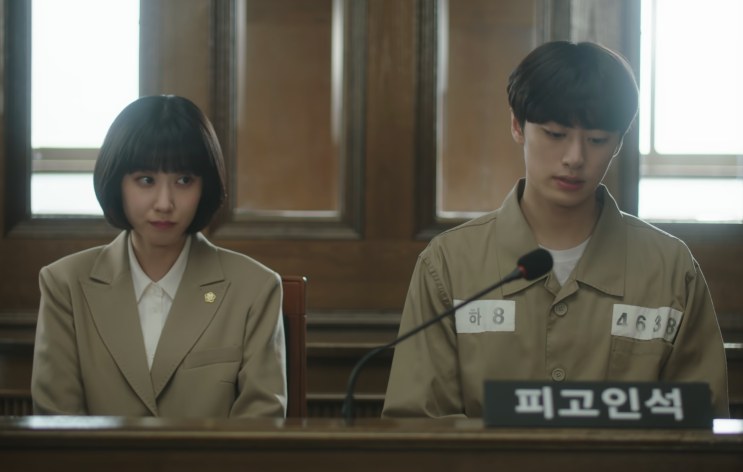 Woo Young-woo e Yang Jeong-il sentados lado a lado no banco dos réus, no tribunal