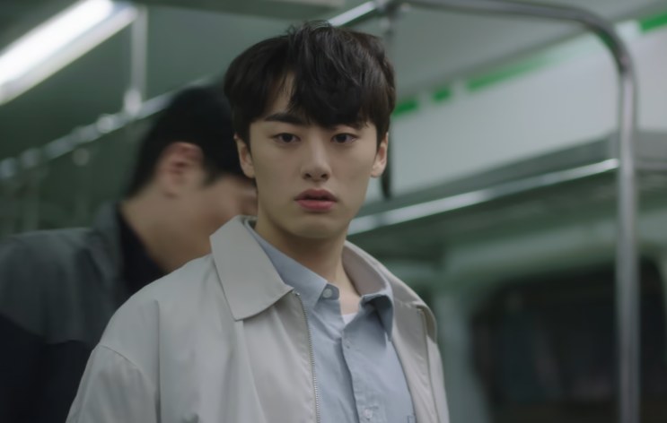 Yang Jeong-il de casaco claro, em pé dentro de um vagão de metrô