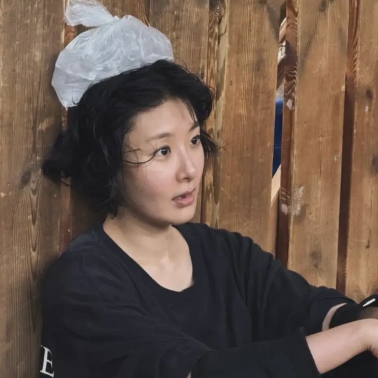 Hyunri de óculos nos bastidores, com touca de proteção no cabelo